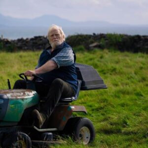 An older man riding a lawn mower in a field.